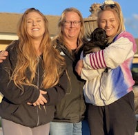 three women standing in front of a house with a dog