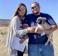 a man and woman holding a puppy in the dirt