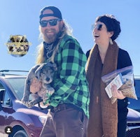 a man and woman holding a dog in front of a car