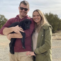 a man and woman holding a black lab puppy