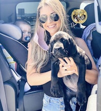 a woman holding a black dog in the back seat of a car