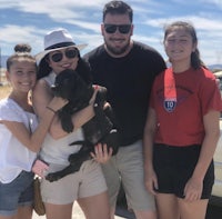 a family holding a black dog in front of a car