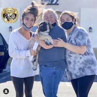 three women with masks holding a puppy in front of a building