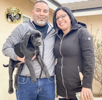 a man and woman standing in front of a house holding a puppy