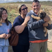 a family holding a puppy in front of a fence